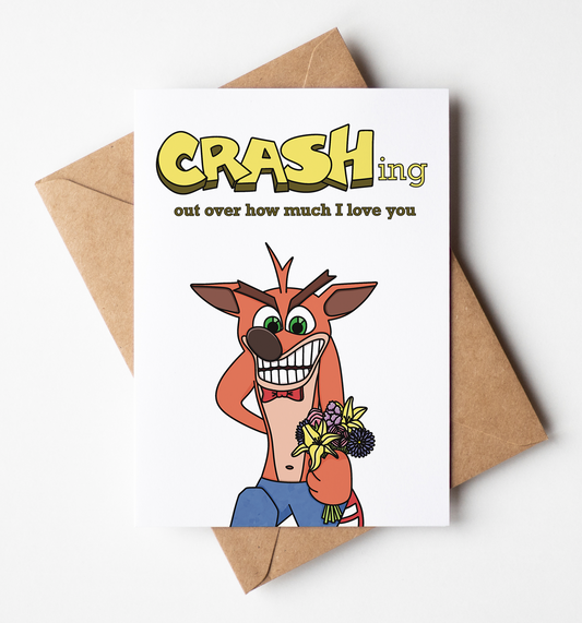 A white greeting card with a Crash Bandicoot-themed design, placed on top of a brown kraft envelope against a clean white background. The card reads 'CRASHing out over how much I love you' with a cartoon Crash holding flowers.