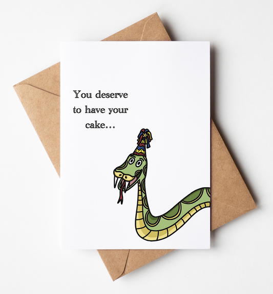 A white greeting card with the text 'You deserve to have your cake and a smiling snake.