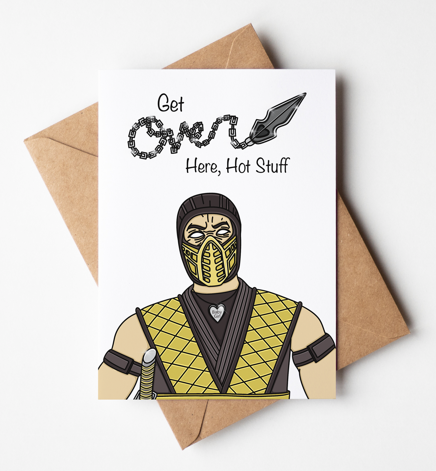 A white greeting card with a brown kraft envelope behind it, featuring a cartoon illustration of a masked figure in a yellow and black diamond-patterned outfit and the text 'Get Over Here, Hot Stuff'.