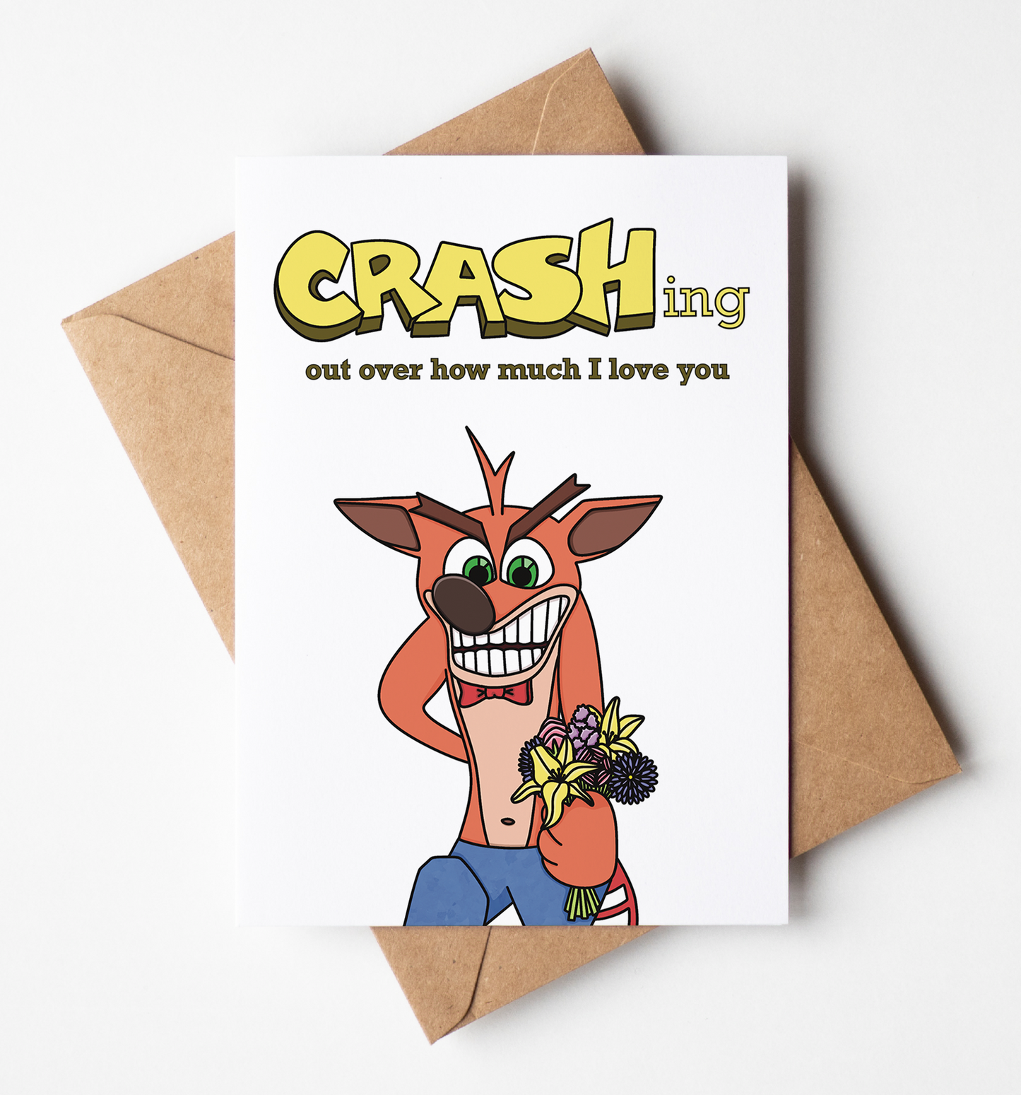 A white greeting card with a Crash Bandicoot-themed design, placed on top of a brown kraft envelope against a clean white background. The card reads 'CRASHing out over how much I love you' with a cartoon Crash holding flowers.
