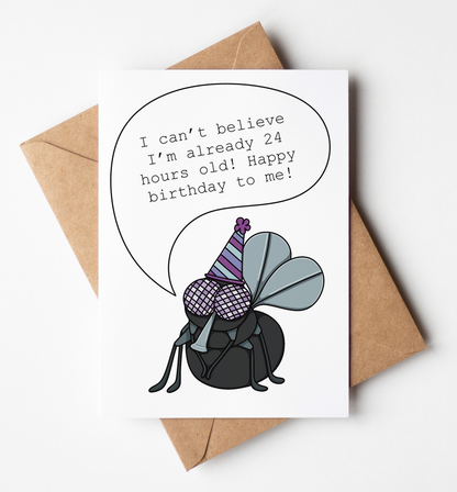 A white greeting card with a brown kraft envelope, featuring a cartoon bug wearing a party hat and a speech bubble that reads, 'I can't believe I'm already 24 hours old! Happy birthday to me!' on a light gray background.