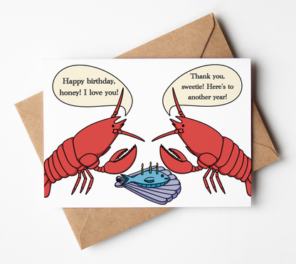 A square greeting card with a humorous lobster illustration and speech bubbles, shown with a brown kraft envelope on a clean white background. Final product contains 3D party hats on each lobster on the front of the card (not shown in picture).