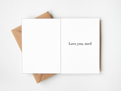 An open white greeting card with the printed phrase 'Love you, nerd' on the right panel, layered over a brown kraft envelope on a clean white background.