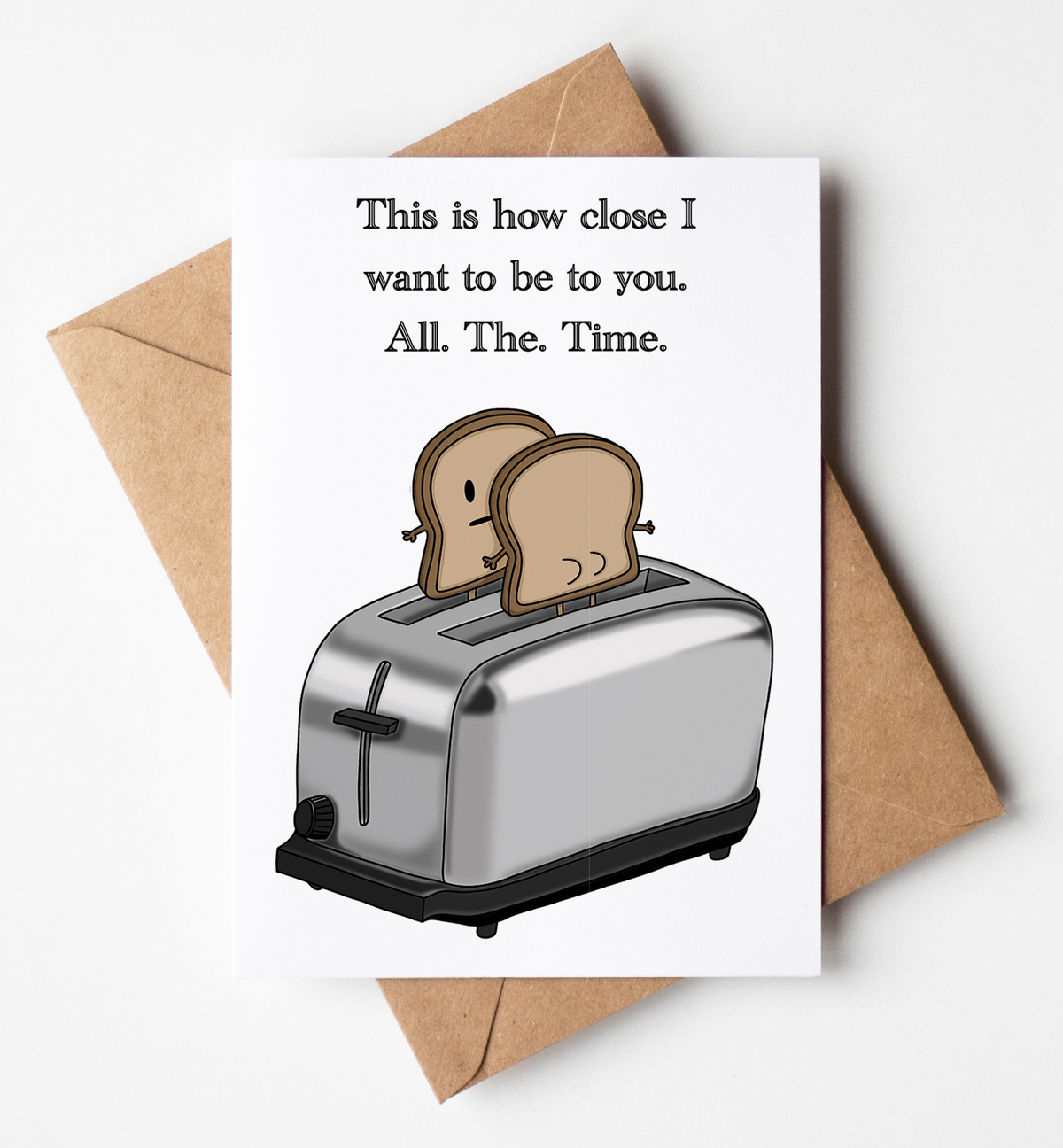 A white greeting card with a humorous quote and an illustration of two slices of toast in a toaster, shown with a brown kraft envelope on a light gray background.