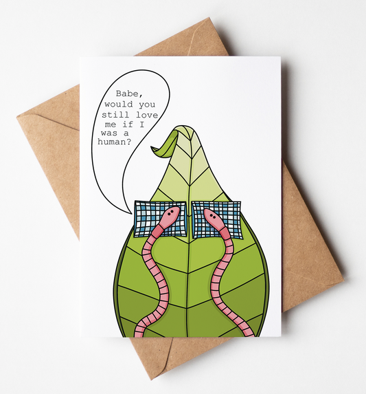 A white greeting card with a humorous illustration of a green leaf-like body, pink snakes, and a speech bubble reading 'Babe, would you still love me if I was a human?' is shown on a light gray background with a brown kraft envelope behind it.